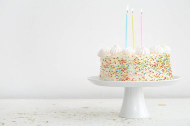 Lezzetli doğum günü pastasıyla beyaz duvarın yanındaki masada dur.