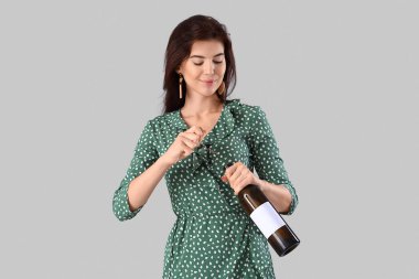 Güzel genç bir kadın arka planda şarap şişesi açıyor.