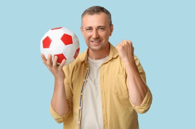 Mavi arka planda futbol topu olan mutlu ve olgun bir adam.