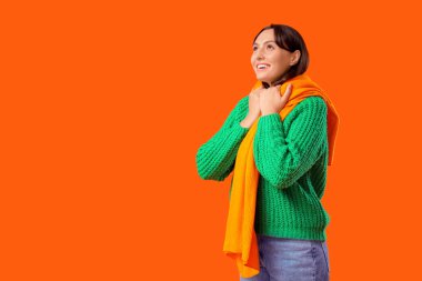 Turuncu arka planda atkısı olan yeşil kazaklı genç bir kadın.