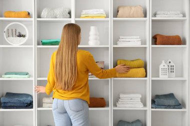Genç bir kadın evdeki raflara giysi yığıyor.