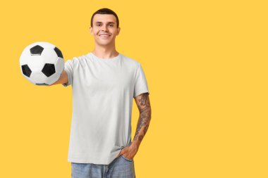 Sarı arka planda futbol topu olan yakışıklı genç adam.