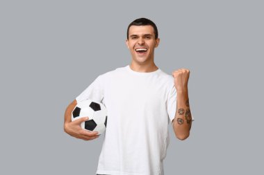 Gri arka planda futbol topu olan yakışıklı genç adam.