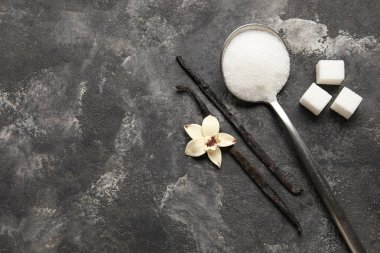 Aromatik vanilya şekerli kaşık, çiçek ve siyah arka planda çubuklar