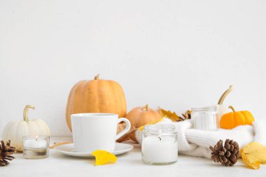 Bir fincan çay, sonbahar yaprakları, kazak, yanan mumlar, kozalaklar ve beyaz arka planda balkabakları.