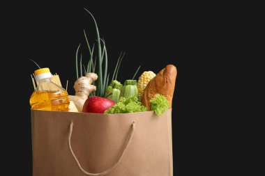 Siyah zemin üzerinde farklı taze ürünler olan kağıt alışveriş torbası.