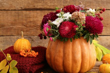 Beautiful autumn bouquet in pumpkin and leaves on wooden background