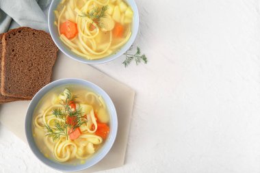 Bowls of tasty chicken soup and bread on white background
