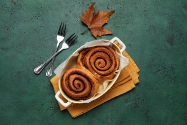 Lezzetli tarçınlı çörekler ve yeşil arka planda sonbahar yaprağı.