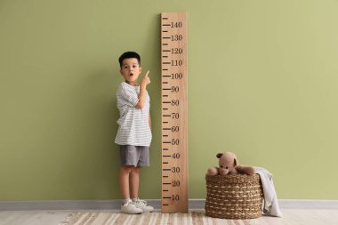 Küçük Asyalı çocuk yeşil duvarın yanındaki stadyumu işaret ediyor.