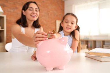 Annesiyle küçük bir kız evdeki domuz kumbarasına para koyuyor.