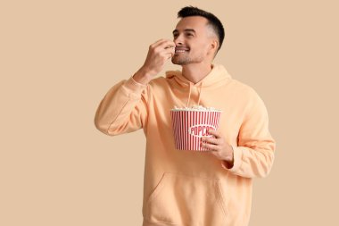 Mutlu genç adam bej arka planda patlamış mısır yiyor.