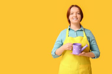 Sarı arka planda sulama tenekesi olan gülümseyen genç kadın.