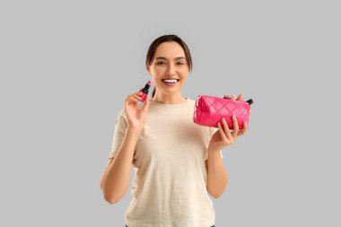 Makyaj malzemeleriyle dolu kozmetik çantası ve gri arka planda ruju olan güzel bir kadın.