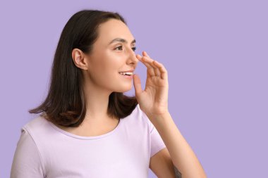 Genç bir kadın leylak arka planda burnuna dokunuyor, yakın plan.