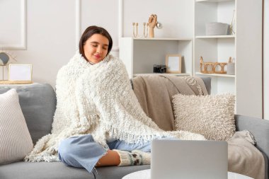 Evdeki kanepede oturan sıcak ekoseli genç kadın.