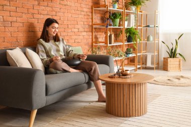 Evdeki kanepede sopayla glukofon çalan genç bir kadın.