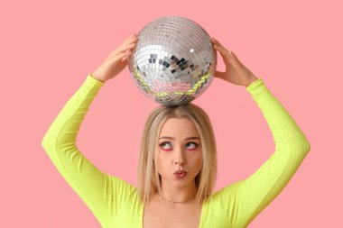 Güzel, düşünceli, genç bir bayan disko topuyla pembe arka planda öpüşüyor.