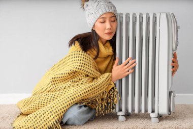 Kışlık giysili genç Asyalı kadın radyatörün yanında.