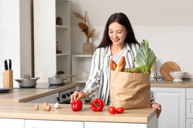 Genç Asyalı kadın mutfaktaki marketten taze ürünleri indiriyor.
