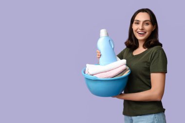 Çamaşır sepeti ve leylak arka planda bir şişe deterjanı olan genç bir kadın.