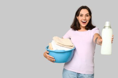 Çamaşır sepeti ve gri arka planda bir şişe deterjanı olan genç bir kadın.