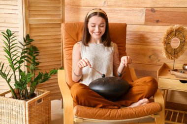 Evdeki koltukta sopayla glukofon çalan genç bir kadın.