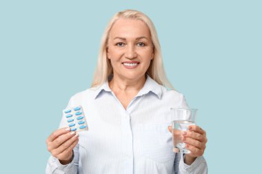 Güzel olgun bir kadın, mavi arka planda haplar ve bir bardak suyla.