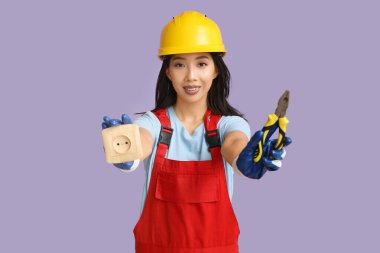 Mor arka planda pense ve soketi olan genç bir elektrikçi kadın.