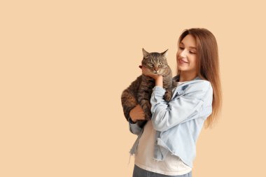 Bej arka planda sevimli tekir kedisi olan güzel genç bir kadın.
