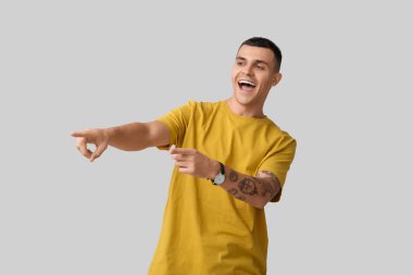 Gri arka planda gülen ve işaret eden mutlu genç bir adamın portresi.