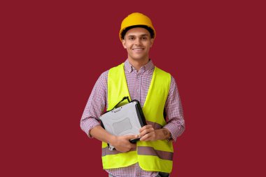 Kırmızı arka planda dizüstü bilgisayarı olan genç erkek mühendis.