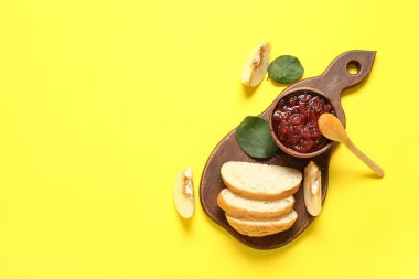 Reçelli ahşap kase, ayva meyvesi ve sarı arka planda ekmek dilimleri.