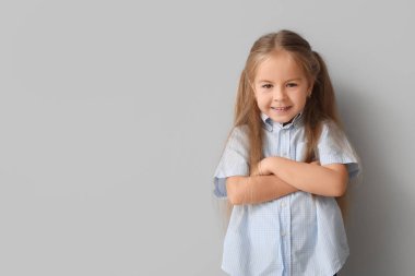 Gri arka planda çapraz kolları olan mutlu küçük kız.