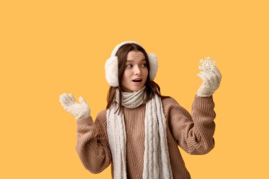 Sarı arka planda dekoratif kar tanesiyle şok olmuş genç bir kadın.