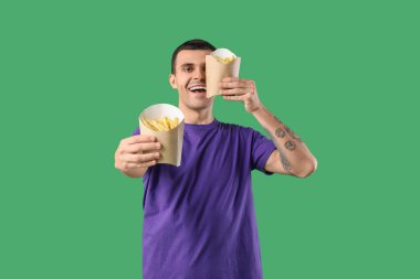 Yeşil arka planda patates kızartması olan genç adam.