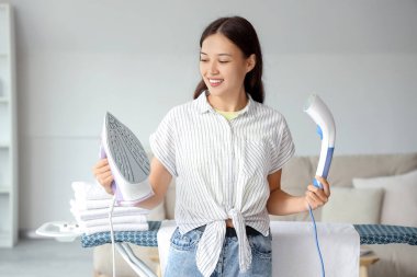 Evde demir ve giysi buharlı genç bir Asyalı kadın var.