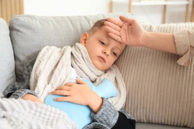 Anne, hasta oğlunun alnına dokunuyor sıcak su şişesiyle evde yatıyor.