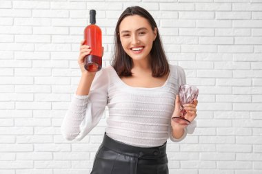 Beyaz tuğlalı arka planda cam ve şarap şişesi olan güzel genç bir kadın.