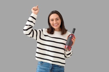 Gri arka planda şarap şişesi olan güzel genç bir kadın.