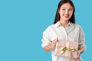 Mavi arka planda hediye kutusu olan güzel bir Asyalı kadın.