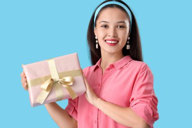 Mavi arka planda hediye kutusu olan güzel bir Asyalı kadın.