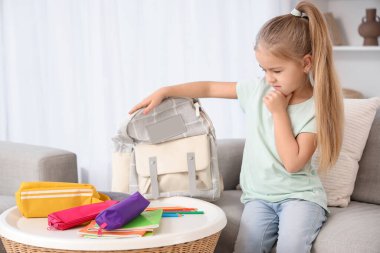 Evdeki masada sırt çantalı ve kalem çantalı düşünceli küçük kız.