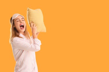 Turuncu arka planda sarı yumuşak yastıklı uyku maskeli güzel bir kadın.