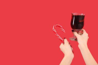 Kırmızı arka planda sıcak şarap ve şeker kamışlı kadın elleri.