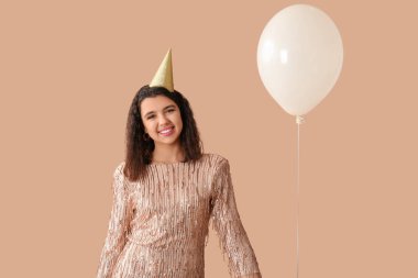 Parti şapkalı güzel bir kadın hava balonuyla kahverengi arka planda doğum gününü kutluyor.