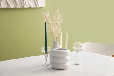 Renk duvarının yanında yanan mumlar, vazolar ve kum saati.