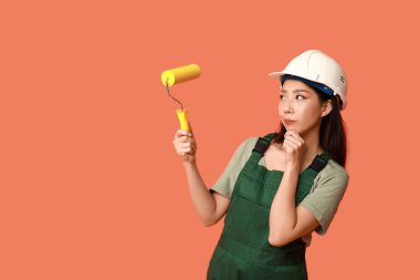 Turuncu arka planda tekerlekli sandalyesi olan Asyalı düşünceli kadın ressam.