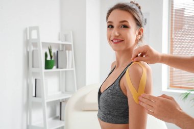 Erkek fizyoterapist rehabilitasyon merkezinde kadının omzuna bant yapıştırıyor.