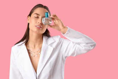 Pembe arka planda parfümü olan zarif bir genç kadın.